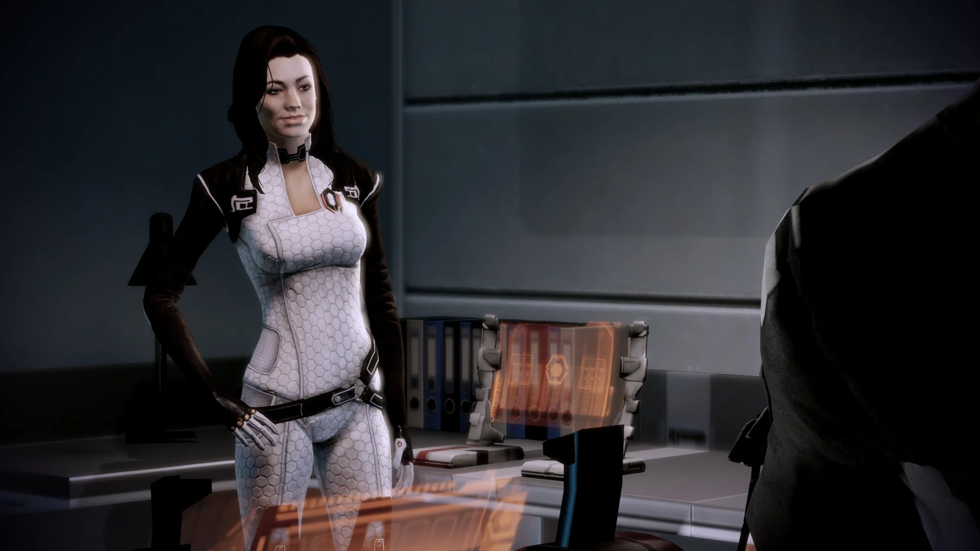 Mass Effect 2 - Miranda Lawson con la mano en la cintura en una sala con panel holográfico
